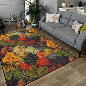 May include: A rectangular area rug with a colorful, abstract design. The rug features a pattern of various colors, including orange, yellow, green, and brown. The rug is placed on a wooden floor in a living room setting.