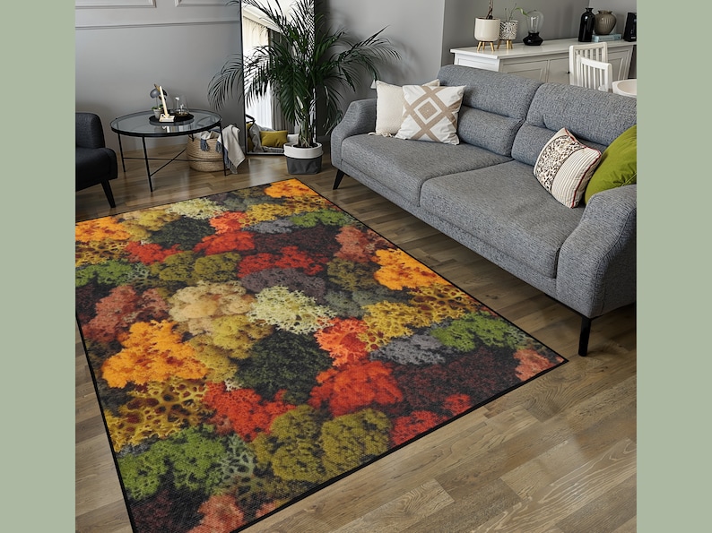 May include: A rectangular area rug with a colorful, abstract design. The rug features a pattern of various colors, including orange, yellow, green, and brown. The rug is placed on a wooden floor in a living room setting.