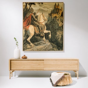 May include: A vintage tapestry featuring a knight riding a white horse towards a medieval castle. The tapestry is framed in a wooden frame and has a detailed background of trees and foliage.