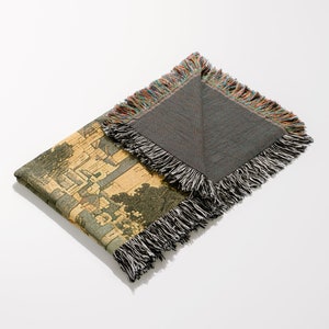 May include: A woven tapestry throw blanket with a colorful fringe border. One side features a detailed illustration of a cityscape, while the other side is a solid gray.