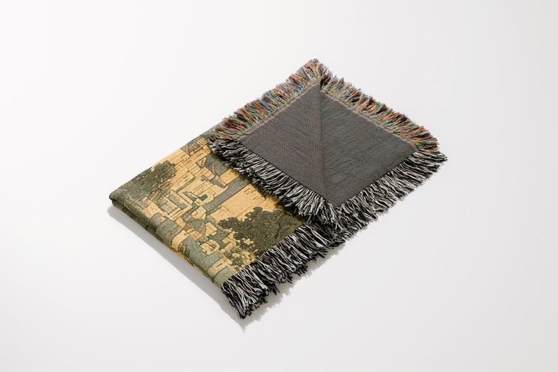 May include: A woven tapestry throw blanket with a colorful fringe border. One side features a detailed illustration of a cityscape, while the other side is a solid gray.