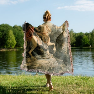 May include: A tapestry throw blanket featuring a detailed image of a knight riding a white horse through a forest. The tapestry is woven with intricate details and rich colors, including shades of brown, green, and gold.