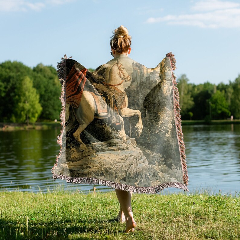May include: A tapestry throw blanket featuring a detailed image of a knight riding a white horse through a forest. The tapestry is woven with intricate details and rich colors, including shades of brown, green, and gold.
