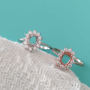 Può includere: Due anelli con montature ovali circondate da piccole pietre trasparenti. L'anello a sinistra è d'argento e l'anello a destra è in oro rosa.