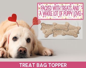 May include: A golden retriever dog wearing a red heart headband looks at the camera. The dog is lying on a white surface. A treat bag topper with the text "Packed with treats and a whole lot of puppy love!" is in the background. The topper has a pink background with white hearts and dog paw prints.