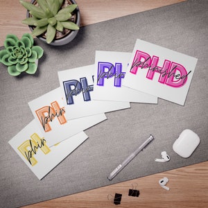 May include: Five white cards with the word "PHinished" written in different colors. The colors are purple, blue, orange, yellow, and pink. The cards are arranged in a fan shape on a gray surface.