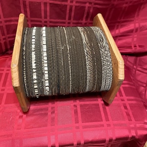May include: A wooden spool with a large roll of black and white braided rope. The spool is made of light brown wood and has a rectangular shape.