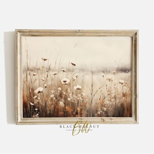 May include: A framed watercolour painting of a field of white wildflowers with a soft, hazy background. The painting is in shades of brown, beige, and white, with a hint of orange in the foreground. The frame is a light wood colour.