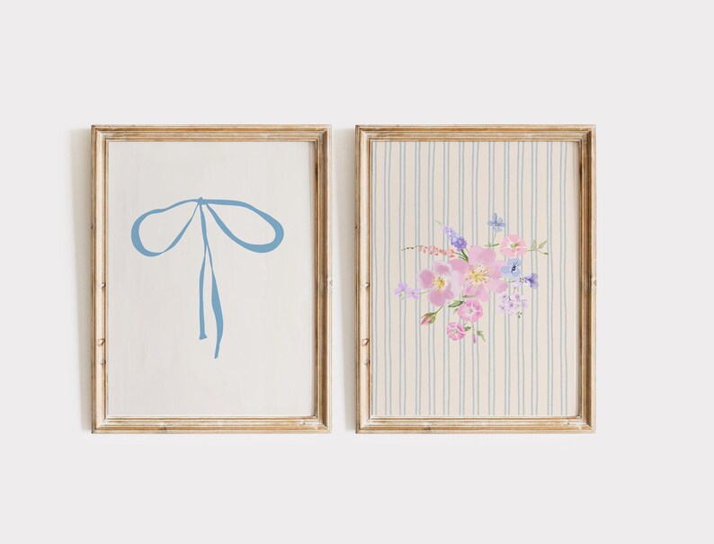 May include: Two framed art prints. One features a light blue bow on a white background. The other print has a floral arrangement in pink and purple hues on a striped background. Both are in gold-toned frames.
