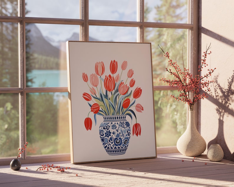 May include: A framed print of a watercolor painting of a bouquet of red and pink tulips in a blue and white patterned vase. The vase is sitting on a table in front of a window with a view of a lake and mountains.