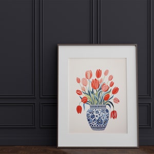 May include: A framed print of a watercolor painting featuring a bouquet of red and pink tulips in a blue and white porcelain vase with a floral pattern.