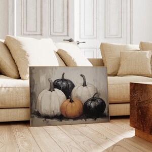 Peut inclure: Une peinture repr&eacute;sentant cinq citrouilles, deux blanches, deux noires et une orange. Les citrouilles sont dispos&eacute;es en rang&eacute;e sur un fond brun clair.
