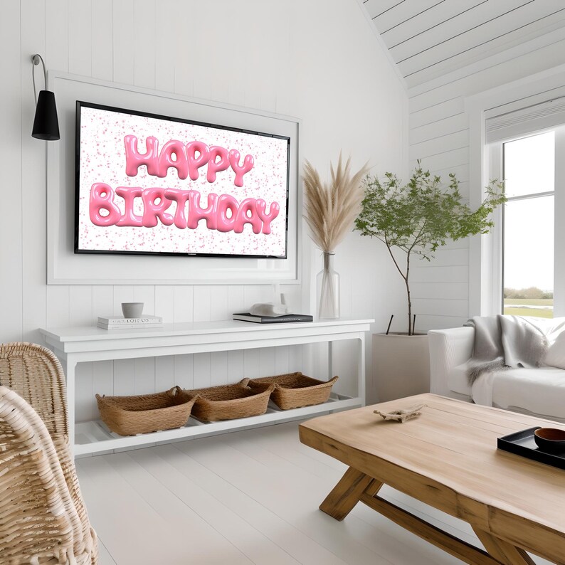 May include: A white television screen displaying the words "Happy Birthday" in pink, 3D letters against a white background with pink confetti. The television is mounted on a white wall in a living room setting.