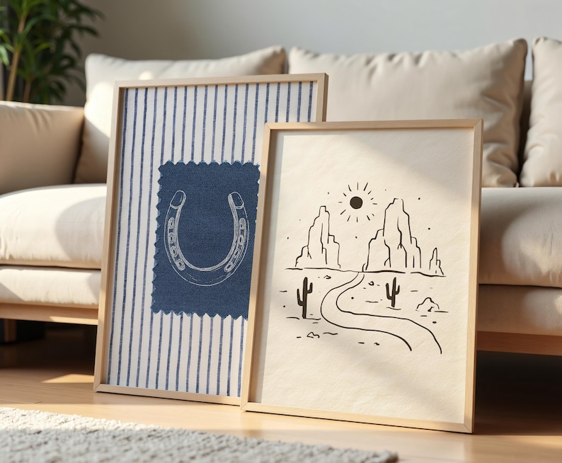 May include: Two framed art prints. One features a horseshoe design on a blue fabric patch over a striped background. The other print depicts a desert landscape with a road, cacti, and mountains, all in black and white.