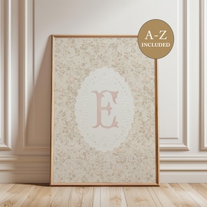 May include: A framed print featuring a floral pattern background with a white oval in the center. The oval contains the letter "E" in a soft pink color. The print is in a wooden frame, and the text "A-Z INCLUDED" is in a gold circle.