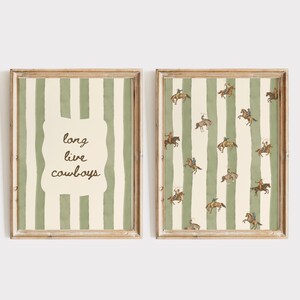 May include: Two framed wall art prints featuring a vertical sage green and cream striped pattern. The left print displays the text long live cowboys in a central cream-coloured shape. The right print features a repeating pattern of cowboys on horses.
