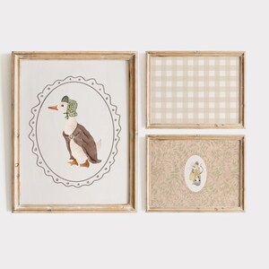 May include: Set of three framed prints. The largest print features a watercolor illustration of a duck wearing a bonnet and vest, set within an oval frame. The other two prints have a gingham pattern and a floral design.