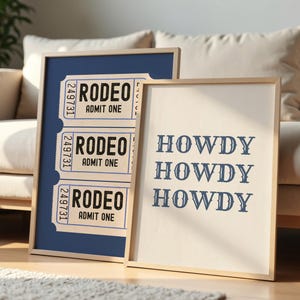 May include: Two framed prints with a western theme. One features three rodeo tickets with the text "RODEO ADMIT ONE". The other print says "HOWDY HOWDY HOWDY" in a serif font. Both prints have a light wood frame.