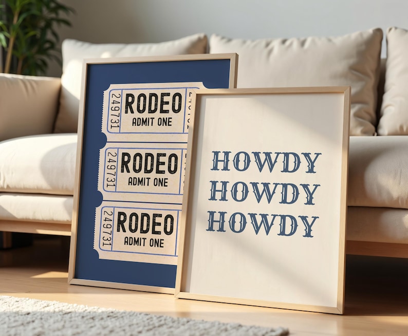 May include: Two framed prints with a western theme. One features three rodeo tickets with the text "RODEO ADMIT ONE". The other print says "HOWDY HOWDY HOWDY" in a serif font. Both prints have a light wood frame.