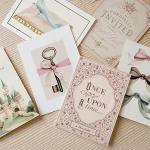 May include: A collection of five rectangular greeting cards featuring illustrations of a glass slipper on a pillow, a royal ball invitation, a key with a pink ribbon, a castle, and a card with the text Once upon a time... a fairytale.