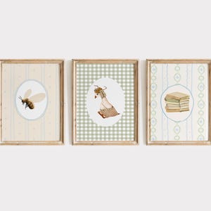 May include: Set of three framed art prints. The prints feature watercolor illustrations of a bee, a goat, and a stack of books, each within an oval frame. The frames are wooden, and the backgrounds have patterned designs in soft colors.