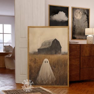 May include: A framed painting of a white ghost standing in a field with a barn in the background. The barn is dark brown and has a wooden door. The field is a light brown color and there are tall grasses in the foreground. The painting is in a gold frame.
