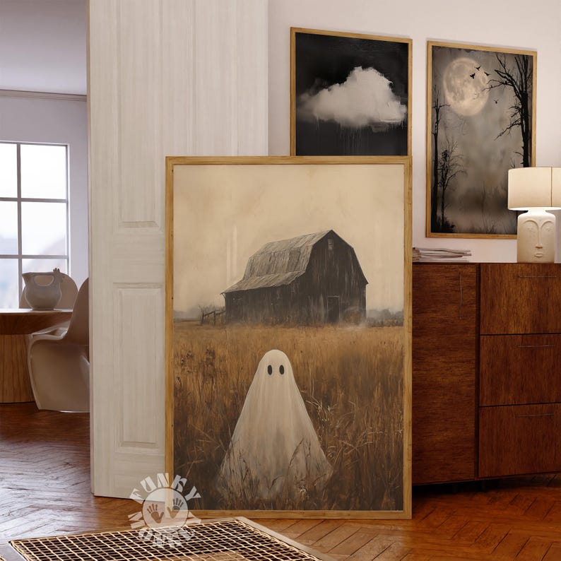 May include: A framed painting of a white ghost standing in a field with a barn in the background. The barn is dark brown and has a wooden door. The field is a light brown color and there are tall grasses in the foreground. The painting is in a gold frame.