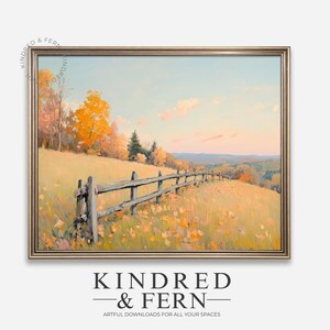 May include: A framed landscape painting showing a field of yellow flowers and a wooden fence. The artwork depicts a tranquil scene with trees in autumn colours under a blue sky. The frame is gold. The text "KINDRED & FERN" is at the bottom.