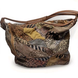 May include: A hobo-style shoulder bag featuring a patchwork design of various animal prints including leopard, zebra, and snakeskin patterns in shades of brown, tan, and black. The bag has a tan leather strap and a side zipper closure.