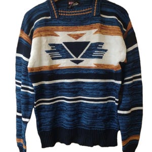 May include: A blue, white, and orange patterned sweater with a geometric design on the front. The sweater has long sleeves and a ribbed hem and cuffs. The sweater is hanging on a wooden hanger.