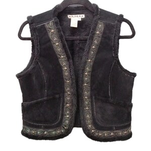 May include: A black sleeveless vest with a faux fur lining and trim. The front features embroidered floral patterns in green and silver thread, accented with small metal studs along the placket and hem. A label reading A.M.I. is at the neck.