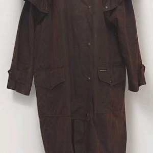 May include: A long, dark brown duster coat featuring a high collar, a shoulder cape, and a front button closure. The coat includes two large flap pockets on the front, long sleeves with adjustable cuffs, and a full-length design with a central vent.