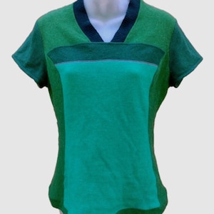 Puede incluir: Una camiseta de manga corta con cuello en V que presenta un diseño de bloques de color con un cuello acanalado verde oscuro, mangas y paneles laterales verde oscuro, y un panel central verde brillante. La prenda tiene una costura horizontal.