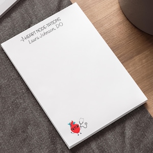 May include: White notepad with the text "HEART NODE-TATIONS Laura Johnson, DO" and a cartoon heart wearing glasses and holding a stethoscope.