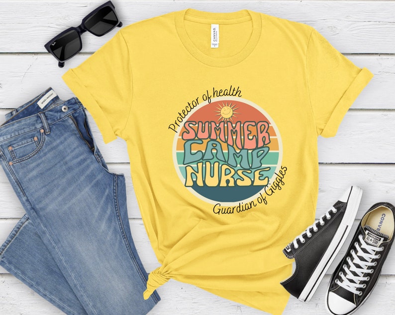 May include: Yellow t-shirt with a retro-style graphic that says "Summer Camp Nurse" in colorful letters. The graphic also includes a sun and a rainbow. The text below the graphic says "Protector of health Guardian of Giggles".