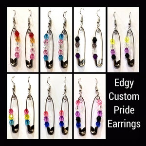 May include: Eight pairs of earrings featuring a safety pin design with colourful crystal beads. The earrings are labelled "Edgy Custom Pride Earrings".