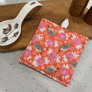 May include: A red and white quilted hot pad with a floral pattern and echidnas. The hot pad has a white loop for hanging.