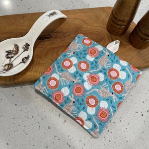 May include: A blue quilted pot holder with a pattern of kangaroos and flowers. The pot holder has a white loop for hanging.