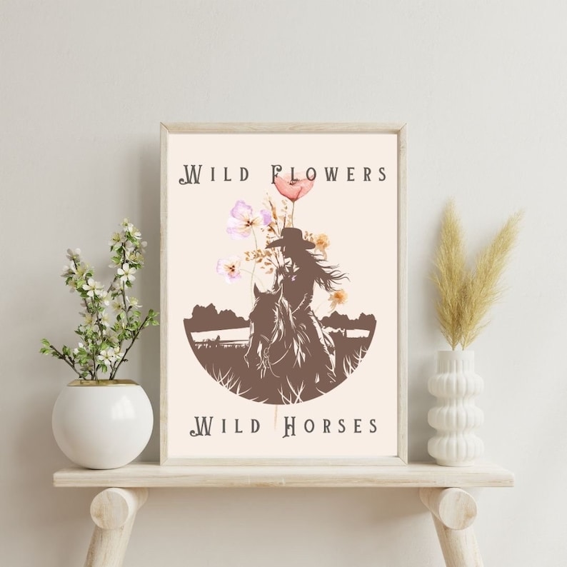 Puede incluir: Un p&oacute;ster beige con una silueta marr&oacute;n de una mujer montando a caballo. La mujer lleva un sombrero de vaquero y el caballo est&aacute; rodeado de flores rosas y blancas. El texto "WILD FLOWERS WILD HORSES" est&aacute; impreso en el p&oacute;ster.