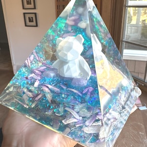 May include: A clear glass pyramid filled with iridescent blue and purple glitter and a white geometric bear figurine.