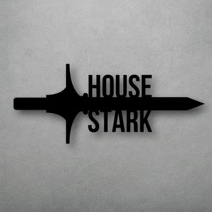 May include: Black metal wall decor featuring a sword with the words "House Stark" on it. The sword is mounted on a gray wall above a wooden table.