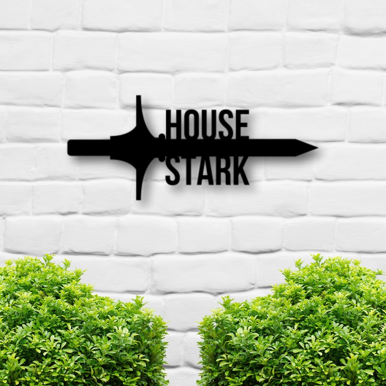 May include: Black metal wall decor featuring a sword with the words "House Stark" on a white brick wall background.
