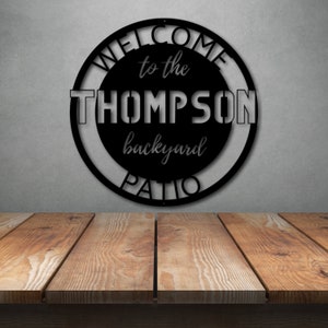 May include: Black metal sign with the text "Welcome to the Thompson backyard patio" in a circle.