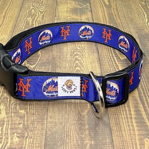 May include: A blue and orange dog collar with a repeating pattern of the New York Mets logo. The collar has a black buckle and a silver D-ring. The collar also has a white tag that says "GIPPY PAWS".