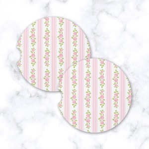 May include: Two round car coasters with a pink and white striped pattern. Vertical rows of pink roses and green leaves are interspersed between the stripes. The coasters have a small notch on one side.