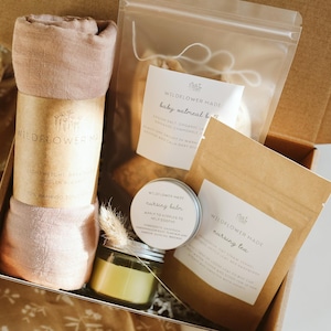 Peut inclure: Un coffret cadeau contenant une mousseline roul&eacute;e rose poudr&eacute; avec une &eacute;tiquette Wildflower Made, un sachet transparent de bain &agrave; l'avoine pour b&eacute;b&eacute;, une petite bo&icirc;te ronde de baume d'allaitement et un sachet en papier brun de tisane.