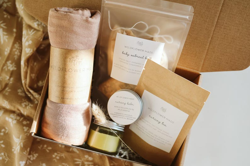 Peut inclure: Un coffret cadeau contenant une mousseline roul&eacute;e rose poudr&eacute; avec une &eacute;tiquette Wildflower Made, un sachet transparent de bain &agrave; l'avoine pour b&eacute;b&eacute;, une petite bo&icirc;te ronde de baume d'allaitement et un sachet en papier brun de tisane.
