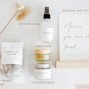 May include: A postpartum care set including four herbal bath bags in a clear pouch, a perineal spray in a clear bottle, a nipple balm in a glass jar with a wooden lid, a calendula salve in a glass jar, and a card reading Mama, you are so loved.
