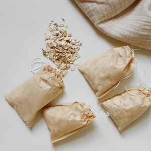 Peut inclure: Quatre petits sachets rectangulaires en papier brun clair avec des fermetures &agrave; cordon blanc, remplis d'avoine s&eacute;ch&eacute;e et de boutons de lavande. Un tas de ce m&ecirc;me m&eacute;lange d'avoine et de lavande est dispos&eacute; &agrave; c&ocirc;t&eacute;, avec un tissu beige.