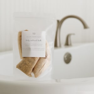 Peut inclure: Un sachet en plastique transparent contenant plusieurs sachets en tissu beige &eacute;tiquet&eacute;s Wildflower Made baby oatmeal bath, listant des ingr&eacute;dients comme le sel d'Epsom, la lavande bio, la camomille bio et l'avoine avec des instructions.